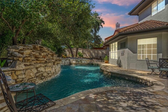 pool at dusk with pool water feature and a patio