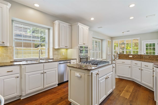 kitchen featuring sink, dark stone countertops, hanging light fixtures, stainless steel appliances, and white cabinets