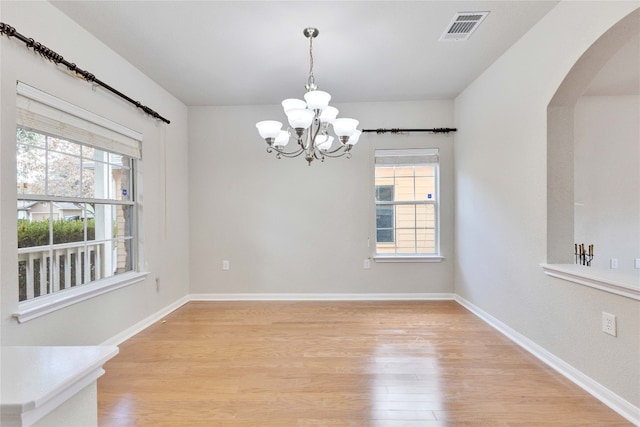 spare room with light wood-type flooring, an inviting chandelier, and plenty of natural light