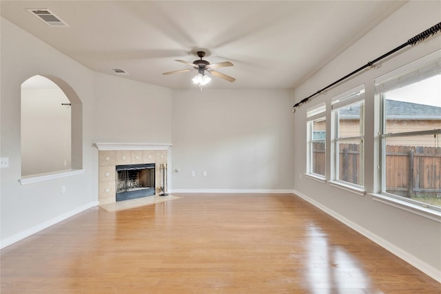 unfurnished living room featuring a tiled fireplace, ceiling fan, light wood-type flooring, and a wealth of natural light