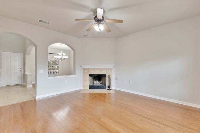 unfurnished living room with a fireplace, ceiling fan with notable chandelier, and light wood-type flooring