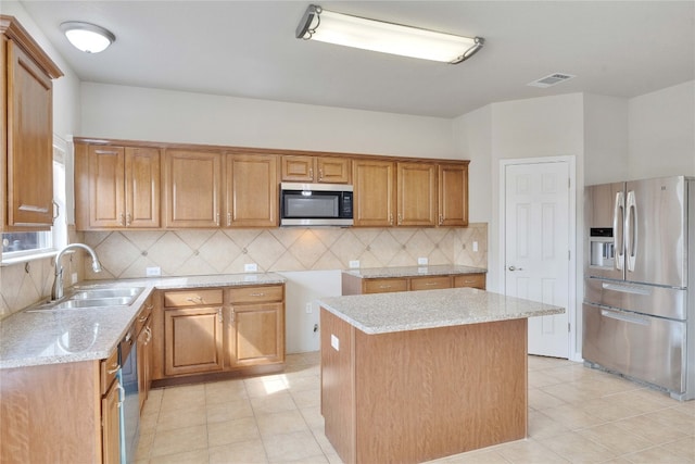 kitchen with appliances with stainless steel finishes, sink, light stone countertops, backsplash, and a center island