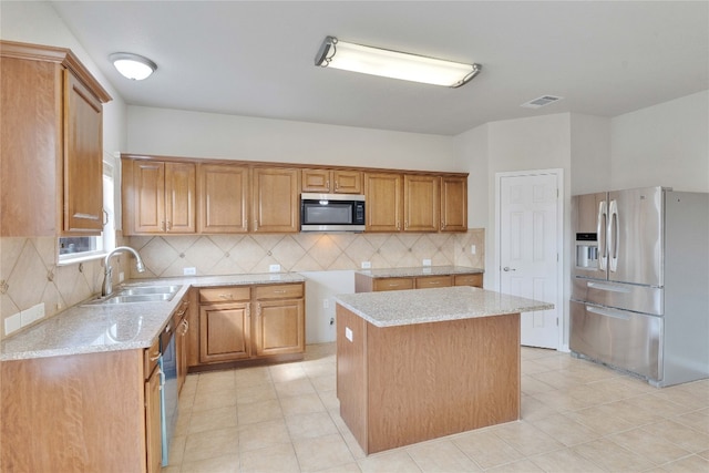 kitchen with tasteful backsplash, appliances with stainless steel finishes, sink, a center island, and light stone counters