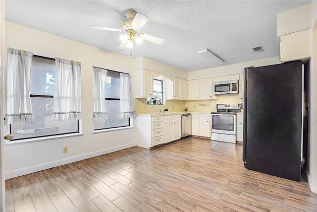 kitchen with sink, a textured ceiling, appliances with stainless steel finishes, and light hardwood / wood-style flooring