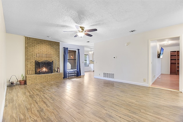 unfurnished living room featuring a textured ceiling, ceiling fan, light wood-type flooring, and a brick fireplace