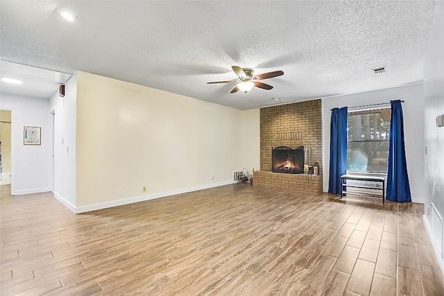 unfurnished living room with light hardwood / wood-style flooring, a textured ceiling, ceiling fan, and a brick fireplace