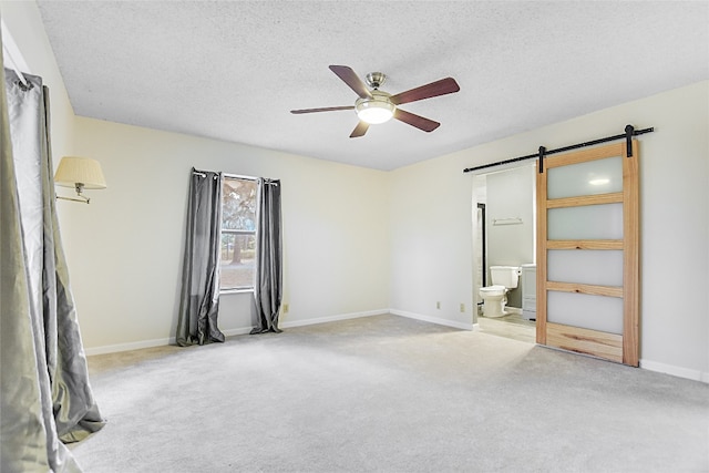 unfurnished bedroom with ensuite bathroom, a barn door, light colored carpet, and ceiling fan