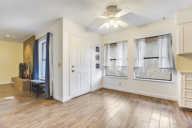 entrance foyer with ceiling fan, a textured ceiling, a brick fireplace, and light wood-type flooring