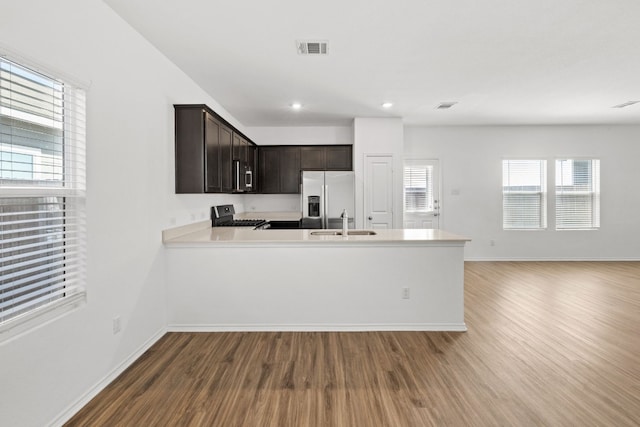 kitchen featuring appliances with stainless steel finishes, sink, light wood-type flooring, kitchen peninsula, and dark brown cabinetry