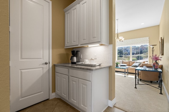 kitchen featuring decorative backsplash, white cabinets, a notable chandelier, and light colored carpet