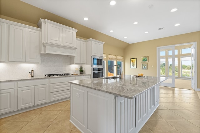 kitchen featuring white cabinets, a center island with sink, light stone countertops, stainless steel appliances, and sink