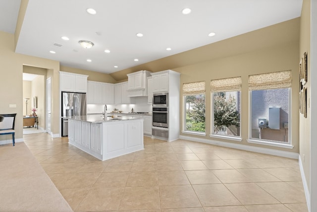 kitchen featuring an island with sink, sink, light tile patterned flooring, white cabinetry, and appliances with stainless steel finishes