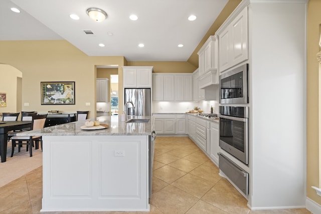 kitchen featuring white cabinetry, light stone countertops, appliances with stainless steel finishes, and a kitchen island with sink