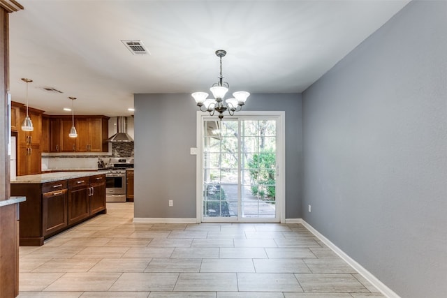 kitchen featuring light stone counters, wall chimney exhaust hood, an inviting chandelier, gas range, and pendant lighting