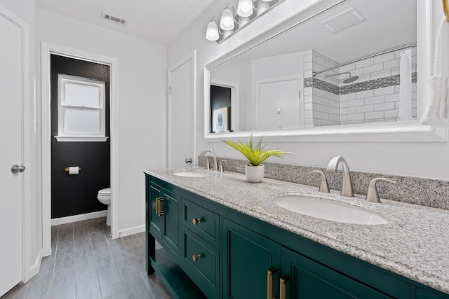 bathroom featuring wood-type flooring, vanity, a tile shower, and toilet