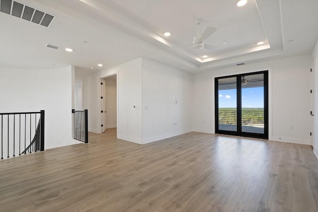 spare room featuring a tray ceiling, ceiling fan, and light wood-type flooring