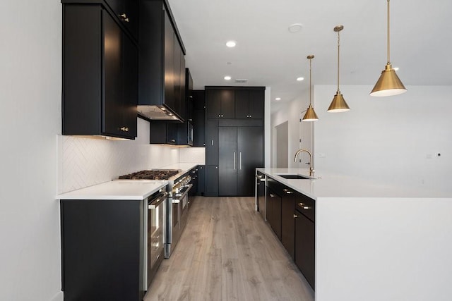 kitchen with decorative backsplash, light wood-type flooring, sink, decorative light fixtures, and stainless steel stove