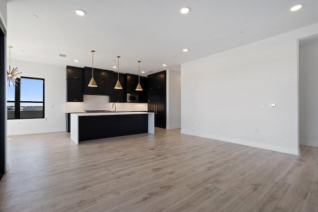 kitchen with sink, backsplash, light hardwood / wood-style floors, decorative light fixtures, and a center island with sink