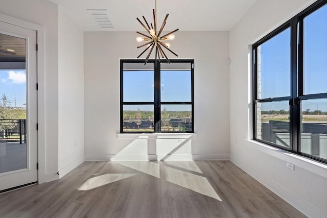 spare room with a wealth of natural light, an inviting chandelier, and hardwood / wood-style flooring