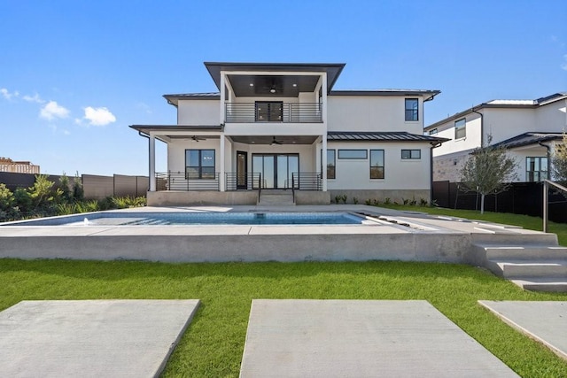 rear view of property with a fenced in pool, ceiling fan, a balcony, and a lawn