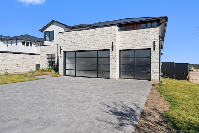 contemporary home with a garage, stone siding, decorative driveway, and a front yard