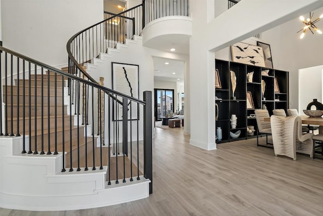 entrance foyer with baseboards, a towering ceiling, wood finished floors, an inviting chandelier, and stairs