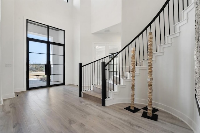 foyer with stairway, wood finished floors, a towering ceiling, and baseboards