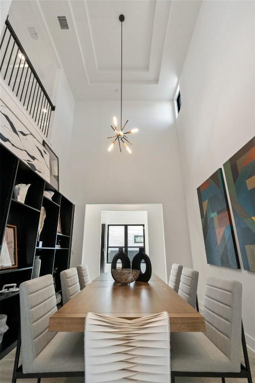 dining space with a notable chandelier, a high ceiling, visible vents, and a tray ceiling