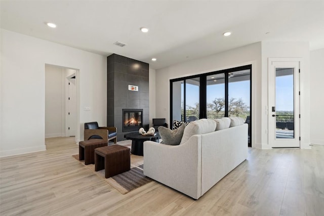 living room with recessed lighting, visible vents, baseboards, light wood-style floors, and a tiled fireplace