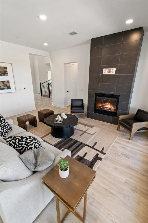 living room featuring baseboards, visible vents, a tiled fireplace, wood finished floors, and recessed lighting