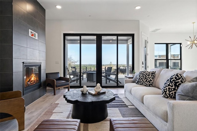 living room featuring a notable chandelier, wood finished floors, a tile fireplace, and recessed lighting