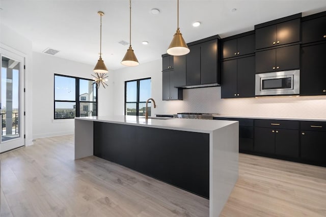 kitchen with light countertops, stainless steel microwave, decorative backsplash, and dark cabinets