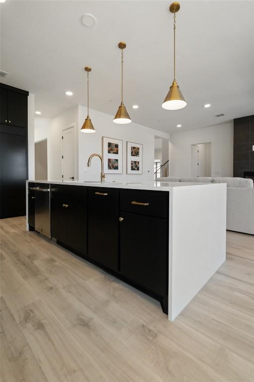 kitchen with a center island with sink, light countertops, dark cabinets, and decorative light fixtures