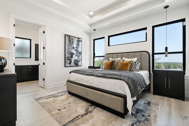 bedroom featuring light wood finished floors, a tray ceiling, ensuite bath, and baseboards