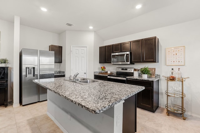 kitchen with appliances with stainless steel finishes, a sink, dark brown cabinetry, and light stone countertops