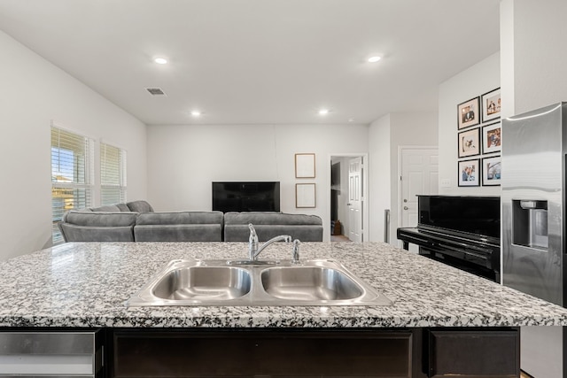 kitchen featuring visible vents, open floor plan, a sink, an island with sink, and stainless steel fridge with ice dispenser