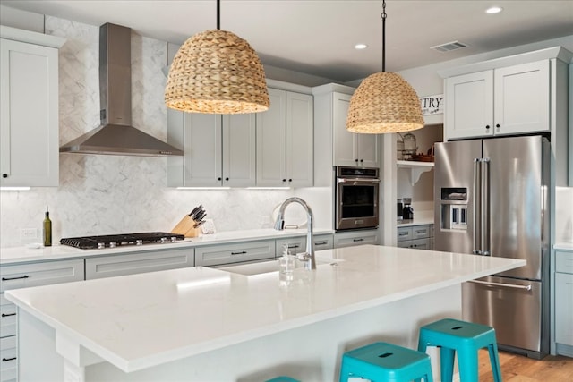 kitchen featuring wall chimney exhaust hood, a kitchen island with sink, a breakfast bar area, and stainless steel appliances