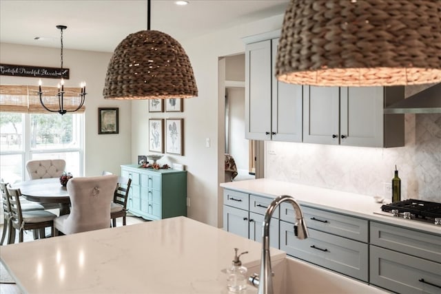 kitchen with decorative backsplash, gray cabinets, a chandelier, and stainless steel gas stovetop