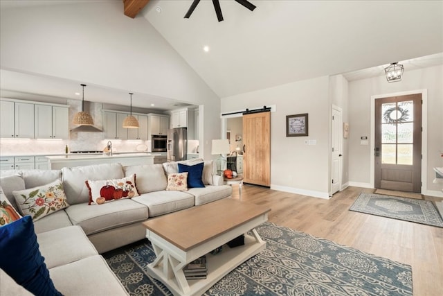 living room featuring beam ceiling, ceiling fan, a barn door, high vaulted ceiling, and light wood-type flooring