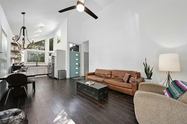 living room with ceiling fan with notable chandelier, dark hardwood / wood-style flooring, sink, and high vaulted ceiling