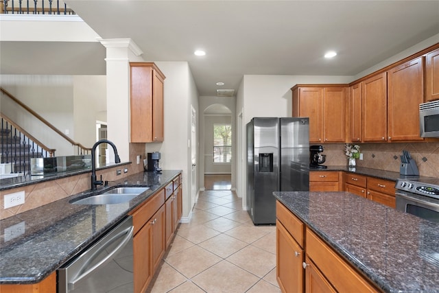 kitchen with appliances with stainless steel finishes, sink, light tile patterned floors, and dark stone counters