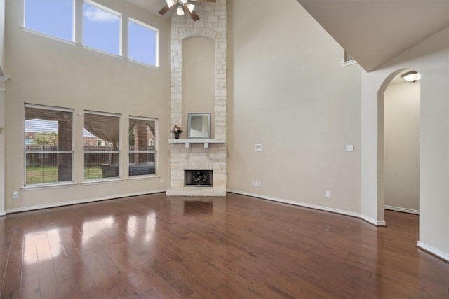 unfurnished living room with ceiling fan, a fireplace, dark hardwood / wood-style flooring, and a towering ceiling