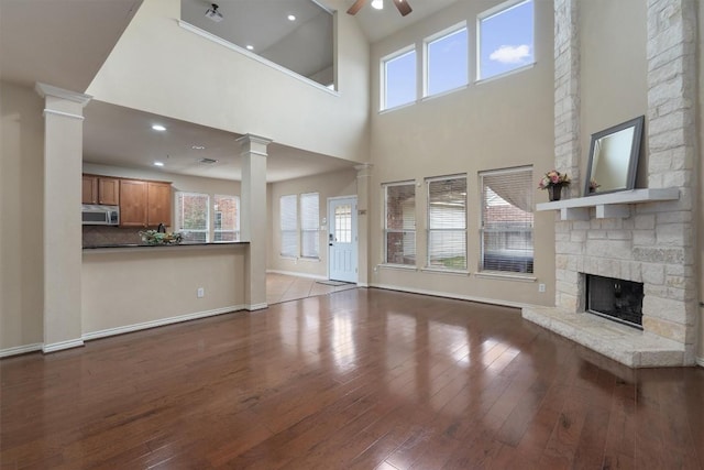 unfurnished living room with ornate columns, a stone fireplace, a high ceiling, ceiling fan, and light hardwood / wood-style floors