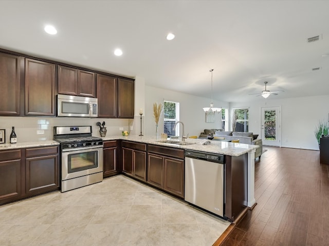 kitchen featuring kitchen peninsula, light wood-type flooring, sink, pendant lighting, and stainless steel appliances