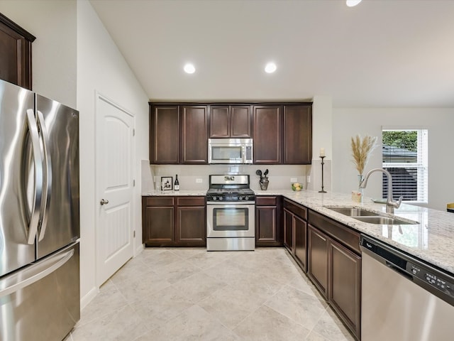 kitchen with kitchen peninsula, dark brown cabinets, sink, light stone countertops, and appliances with stainless steel finishes