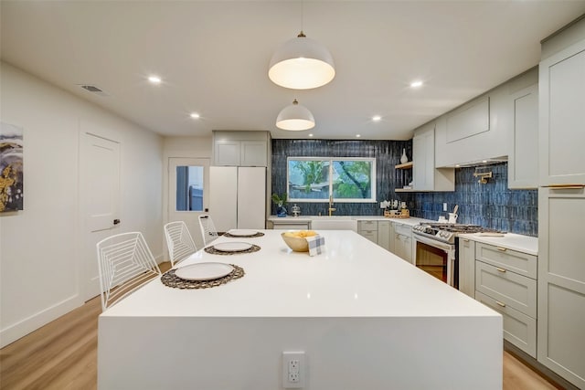 kitchen with hanging light fixtures, a center island, white refrigerator, stainless steel range with gas cooktop, and light hardwood / wood-style floors