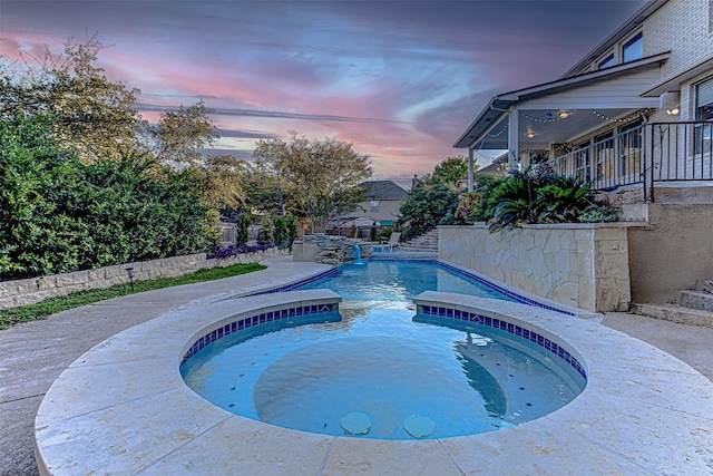 pool at dusk featuring an in ground hot tub