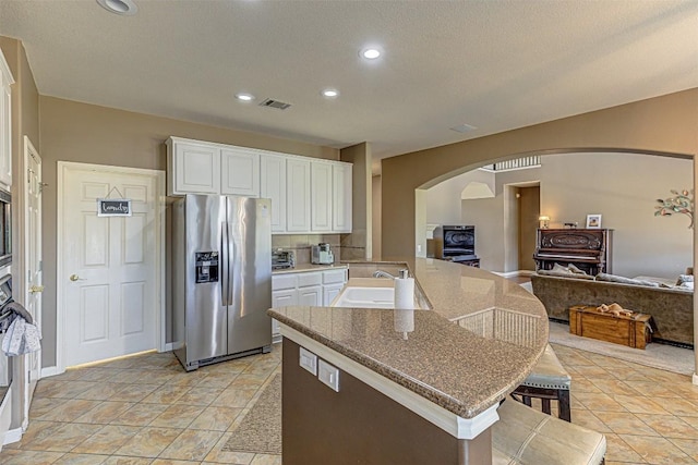 kitchen featuring a kitchen breakfast bar, stainless steel refrigerator with ice dispenser, arched walkways, white cabinets, and a sink