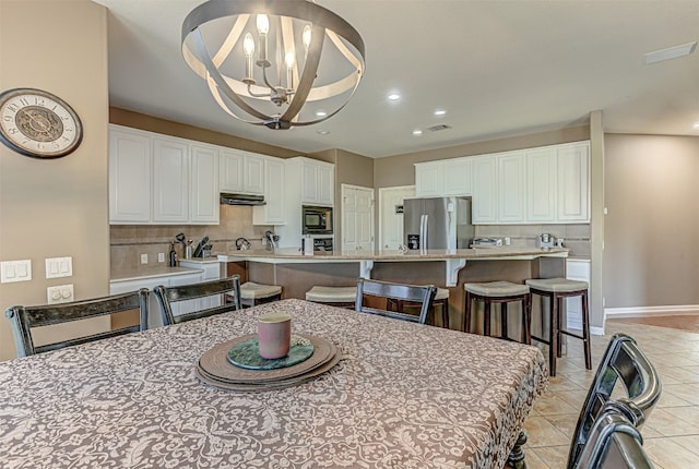 kitchen with stainless steel refrigerator with ice dispenser, backsplash, built in microwave, decorative light fixtures, and white cabinets