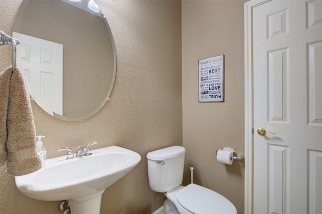 half bathroom with a sink, toilet, and a textured wall